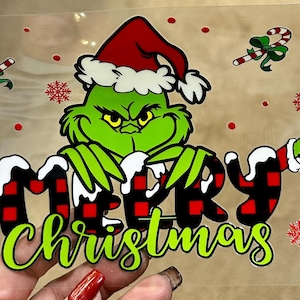 May include: A clear sheet featuring a Grinch design with the words "MERRY Christmas". The Grinch is green and wears a Santa hat. Candy canes, snowflakes, and ornaments are also included in the design.