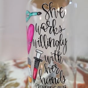 Könnte beinhalten: Klarer Glasbecher mit Bambusdeckel. Der Becher ist mit einer türkisfarbenen Gitarre, einem rosa Herz und einer Spritze verziert. Der Text lautet "She works willingly with her hands" und "Proverbs 31:13".