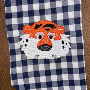 May include: Embroidered orange and black tiger face on a white and navy blue gingham fabric.