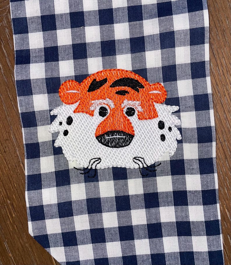 May include: Embroidered orange and black tiger face on a white and navy blue gingham fabric.