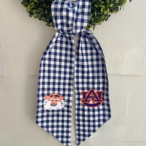 May include: A blue and white gingham ribbon with an embroidered Auburn University logo and a cartoon tiger on one side.