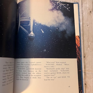 Op de afbeelding: Een open boekpagina met een dramatische illustratie van een ruimteschip en een gaswolk. Tekst op de pagina beschrijft een sciencefiction-sc&egrave;ne met de personages V.I.N.CENT en B.O.B. Het paginanummer 49 is zichtbaar.