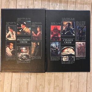 Op de afbeelding: Twee open boekpagina's met afbeeldingen van personages en robots uit een sciencefictionfilm. De linkerpagina is gelabeld met "PALOMINO CREW" en de rechterpagina met "CYGNUS CREW". Elke pagina heeft verschillende afbeeldingen van mensen en robots.