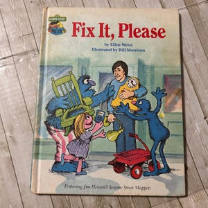 May include: A vintage Sesame Street children's book titled "Fix It, Please." The cover features illustrations of Sesame Street Muppets, including the blue monsters, a girl, and a man holding a clock. The book's title is in red, with the author and illustrator's names below.