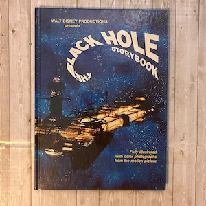 Op de afbeelding: Een vintage hardcover boek getiteld "The Black Hole Storybook" van Walt Disney Productions. De omslag toont een ruimtesc&egrave;ne met een ruimteschip en de titel in wit en blauw tegen een donkerblauwe achtergrond.