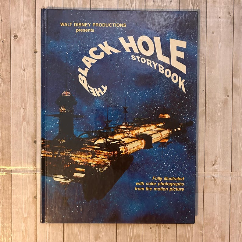 Op de afbeelding: Een vintage hardcover boek getiteld "The Black Hole Storybook" van Walt Disney Productions. De omslag toont een ruimtesc&egrave;ne met een ruimteschip en de titel in wit en blauw tegen een donkerblauwe achtergrond.