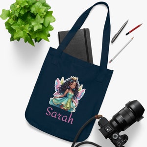 Könnte beinhalten: Eine marineblaue Tragetasche mit einer bunten Feen-Illustration und dem Namen "Sarah" in rosa gedruckt. Die Fee hat braunes Haar, eine Krone und Flügel.