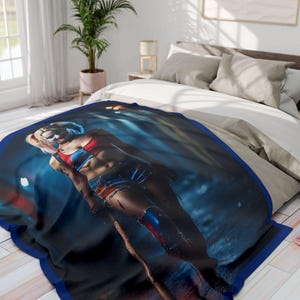 Könnte beinhalten: Eine blaue und schwarze Fleece-Decke mit einem aufgedruckten Bild einer Frau in einem roten und blauen Kostüm, die einen Baseballschläger hält. Die Frau steht in einer dunklen, urbanen Umgebung.