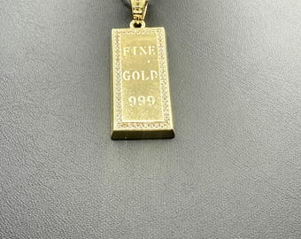 May include: A gold-colored pendant necklace featuring a rectangular bar design. The pendant is inscribed with "FINE GOLD 999" and is embellished with small, clear stones around the edges. The chain is a delicate, twisted rope style.