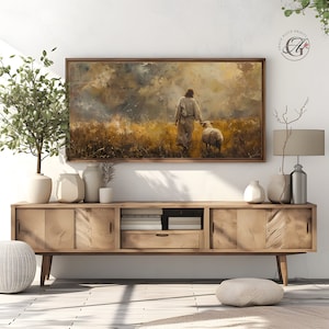 May include: A painting of a man in a white robe walking with a sheep in a field. The sky is cloudy and the sun is shining through the clouds. The painting is framed in a wooden frame.