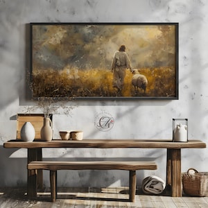 May include: A painting of a man in a white robe walking through a field with a sheep. The sky is cloudy and the sun is shining through the clouds. The painting is framed in a black frame and is hanging on a wall.