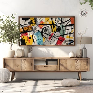 Puede incluir: Impresión de arte abstracto con líneas y formas negras, blancas, amarillas, rojas, azules y verdes sobre un fondo crema. La impresión está enmarcada en un marco de madera marrón y está colgada en una pared blanca sobre un gabinete de madera.