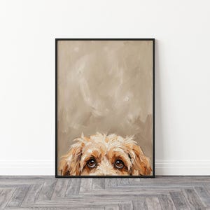 Puede incluir: Impresión artística enmarcada que muestra la cara de un perro. El perro tiene pelo marrón claro y ojos marrones oscuros. El fondo es de color beige con pinceladas. El marco es negro.