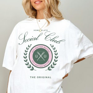 May include: White t-shirt with a green and pink baseball-themed graphic that says "Social Club" and "The Original".