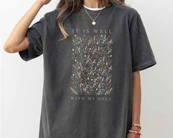 May include: A charcoal gray t-shirt with a floral design and the text "It is well with my soul".