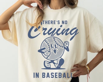 May include: A cream-colored t-shirt with a blue baseball graphic and the text "There's No Crying In Baseball".