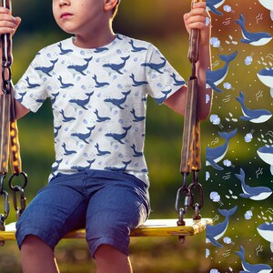 K&ouml;nnte beinhalten: Ein Kind tr&auml;gt ein wei&szlig;es T-Shirt mit einem blauen Walmuster. Das Shirt hat einen Rundhalsausschnitt und kurze &Auml;rmel. Das Kind sitzt auf einer gelben Schaukel.