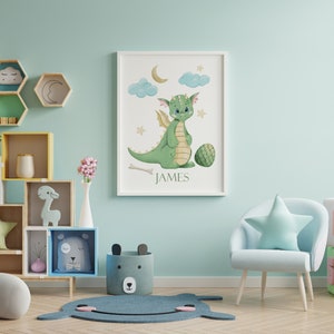 May include: A light blue armchair with a star-shaped pillow sits in a nursery with a green dragon watercolor print on the wall. The print has the name "JAMES" at the bottom.
