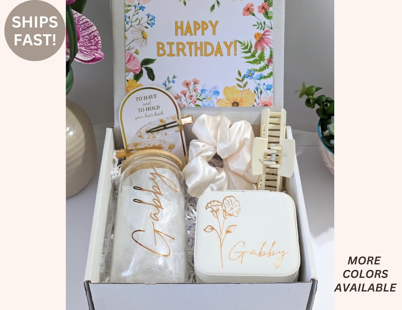 May include: A gift box with a floral "Happy Birthday" card, a jar with "Gabby" in gold script, a white jewelry box with a floral design, a hair claw clip, and a scrunchie. The box also contains a hair clip and a small card.