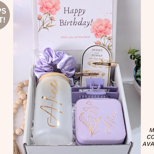 May include: A gift box with a birthday theme, containing a frosted glass with "Alice" in gold script, a lavender scrunchie, hair clips, and a lavender box with a floral design. The box includes a card that says "Happy Birthday!"