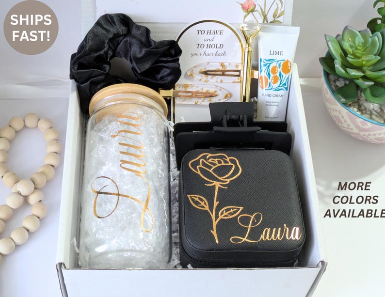 May include: A gift box containing a variety of items. Includes a glass jar with a wooden lid, a black scrunchie, hair clips, a black jewelry box with a gold rose design, and a tube of hand cream. The box is white.