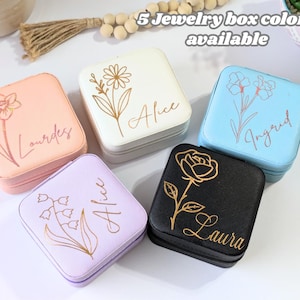 May include: Five square jewelry boxes in various colors: peach, white, light blue, lavender, and black. Each box features a floral design and a name in gold script. The text "5 Jewelry box colors available" is at the top.