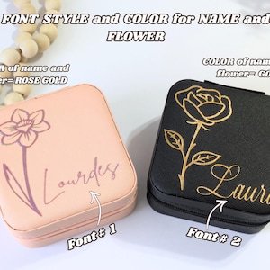 May include: Two square jewelry cases, one peach and one black. The peach case has a rose gold daffodil and the name "Lourdes" in a script font. The black case features a gold rose and the name "Laura".