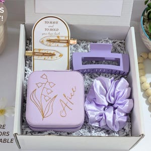 May include: A gift box containing a light purple hair claw clip, scrunchie, and jewelry box with the name "Alice" and floral design. Includes two gold-toned hair clips and the text "TO HAVE and TO HOLD your hair back".