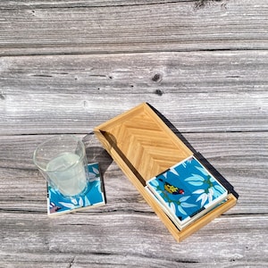 May include: A set of four blue and white coasters with a bird and floral design, stacked on a wooden tray with a chevron pattern.