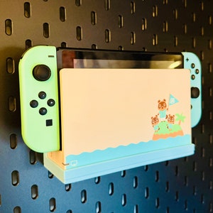 Puede incluir: Una consola Nintendo Switch azul claro y verde con un diseño personalizado de Animal Crossing: New Horizons. La consola está montada en una pared de tablero de clavijas.