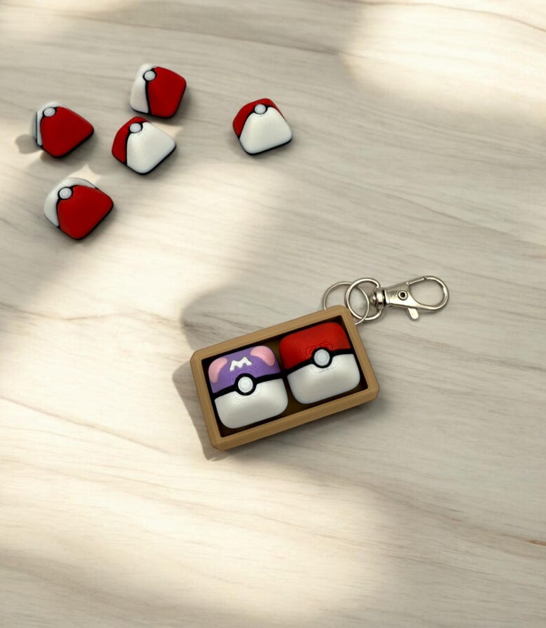May include: A brown wooden keychain with two Poke Balls. One Poke Ball is red and white, the other is purple and white with an 'M' on it.