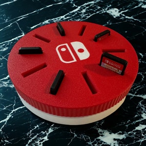 May include: Red and white circular game cartridge holder with slots for multiple cartridges. The holder features the Nintendo Switch logo and is made of foam.