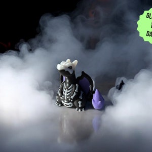 Könnte beinhalten: Eine schwarze und weiße Skelett-Drachenfigur mit violetten Flügeln, die im Dunkeln leuchtet. Der Drache sitzt auf einer weißen Oberfläche mit einem nebligen Hintergrund.