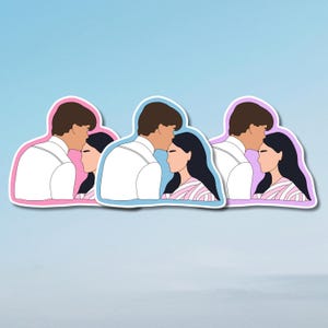 Può includere: Tre adesivi raffiguranti una coppia in un tenero abbraccio. L'uomo indossa una camicia bianca e la donna ha lunghi capelli neri e una camicia a righe rosa e bianche. Ogni adesivo ha un contorno di colore diverso: rosa, blu e viola.