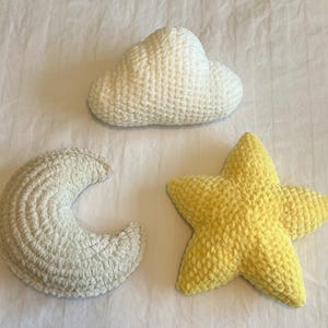 May include: Three crocheted plush toys: a white cloud, a beige crescent moon, and a yellow star. The toys are made with a soft, textured yarn.