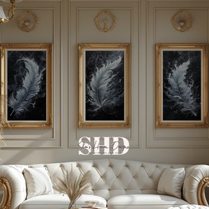 May include: Three gold-framed paintings with black backgrounds and white feather designs hang on a wall in a living room. A white tufted sofa with gold accents sits in front of the paintings. A gold coffee table and a white tufted ottoman are in front of the sofa.