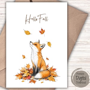 May include: A greetings card featuring a hand-drawn illustration of an orange and white fox sitting amidst a pile of colourful autumn leaves. The fox looks upwards at falling leaves. The text "Hello Fall" is written in brown script at the top.