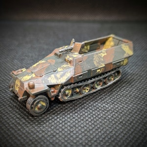 May include: A detailed model of a German half-track armored vehicle, painted in a camouflage pattern of brown, green, and yellow. The model features a detailed interior and a working suspension.
