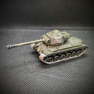 May include: A green toy tank with a detailed turret and tracks. The tank has a long barrel and is made of plastic.