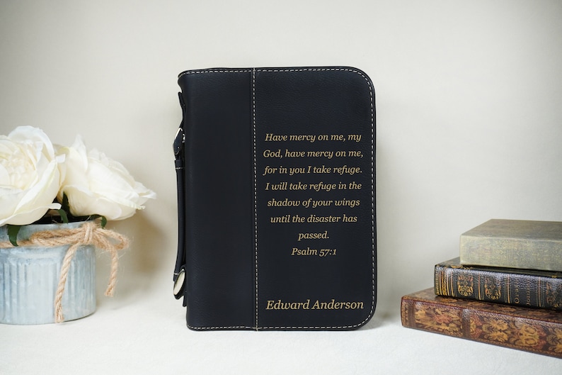 May include: Black leather Bible cover with a gold inscription that reads "Have mercy on me, my God, have mercy on me, for in you I take refuge. I will take refuge in the shadow of your wings until the disaster has passed. Psalm 57:1" and the name "Edward Anderson".