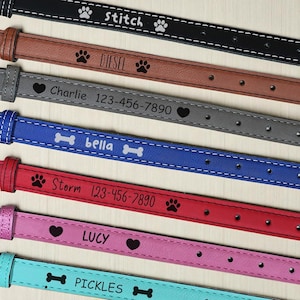 May include: A collection of personalized dog collars in various colors, including black, brown, gray, blue, red, pink, and teal. Each collar features a name and phone number, along with paw prints, hearts, or bone designs.