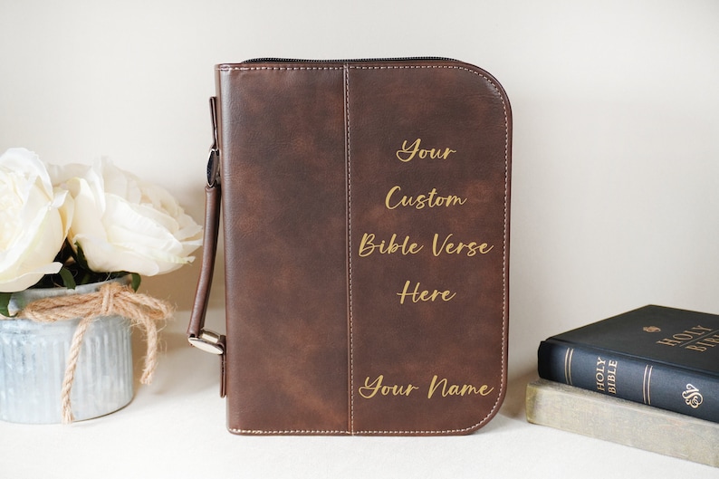 May include: Brown faux leather Bible cover with a zipper closure and a handle. The cover is personalized with gold lettering that reads "Your Custom Bible Verse Here Your Name".