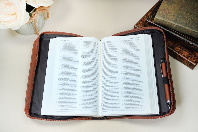 May include: A brown leather zippered Bible case with a black interior. The case is open and a Bible is inside. A pen is in the zippered pocket on the right side of the case.