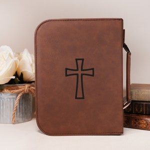 May include: A brown faux leather Bible cover with a black cross design and a handle.