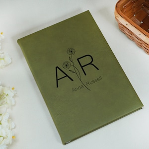 May include: A green leather journal with the initials "A.R." and the name "Anna Russell" embossed in black. The initials are surrounded by a simple floral design.