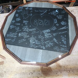 May include: A black octagonal tabletop with a glass top, covered in handwritten messages and drawings, including a heart with the date "8/21/21" and the words "Team Davis! Married!"