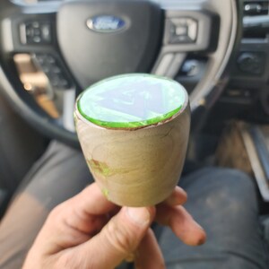 May include: A close-up of a wooden gear shift knob with a green epoxy resin top. The resin has a swirl pattern and is clear in the centre.