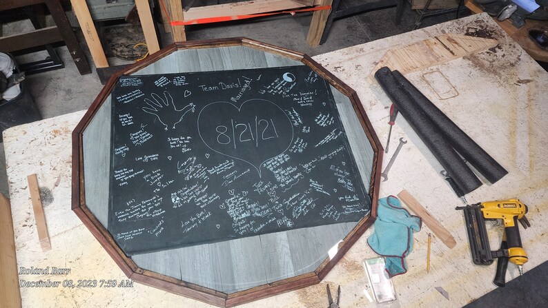 May include: An octagonal sign with a black background and white writing, framed in wood. The sign features a large heart with the date "8/12/21" inside. The text "Team Davis" is written at the top of the sign.
