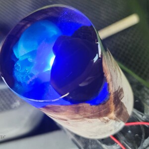 May include: A close-up of a blue and black resin cast inside a wooden cylinder. The resin is clear and has a blue and black swirl pattern. The wood is brown and has a natural grain.
