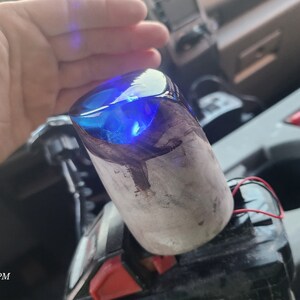 May include: A close-up of a blue resin gear shift knob with a wood base. The knob is illuminated with a bright blue light.